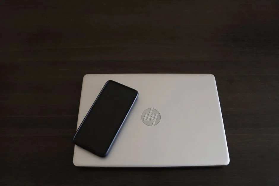 Smartphone liegt auf einem Laptop, Büroarbeitsplatz mit technischen Geräten