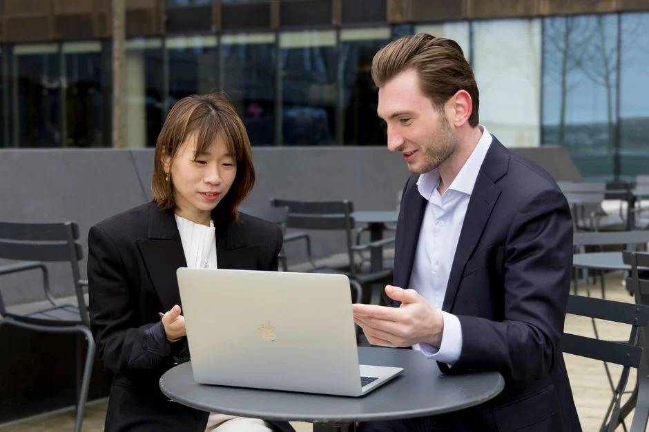 Zwei Personen besprechen an einem Tisch mit Laptop den Umfang eines Website-Angebots