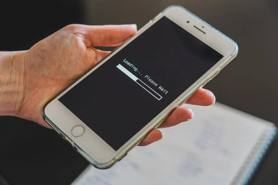 Hand hält ein Smartphone, auf dem ein Ladebalken mit Wartehinweis angezeigt wird