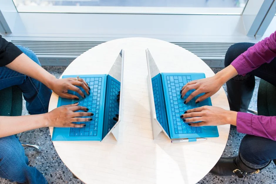 Zwei Personen arbeiten an einem runden Tisch gleichzeitig an eigenen Laptops