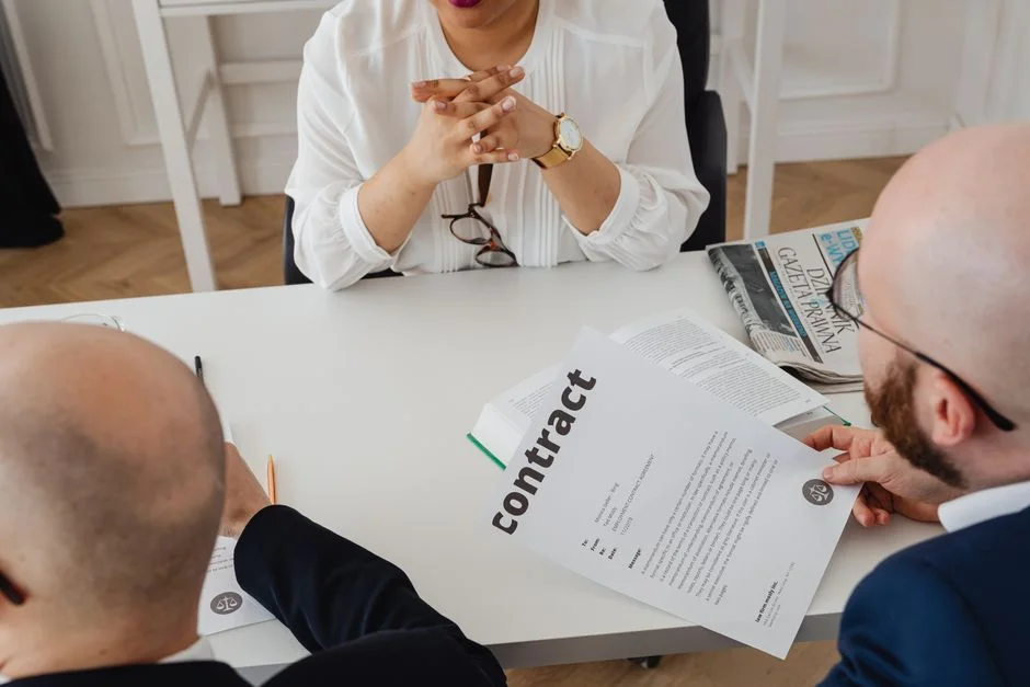 Drei Personen sitzen an einem Besprechungstisch und gehen gemeinsam einen Vertrag durch