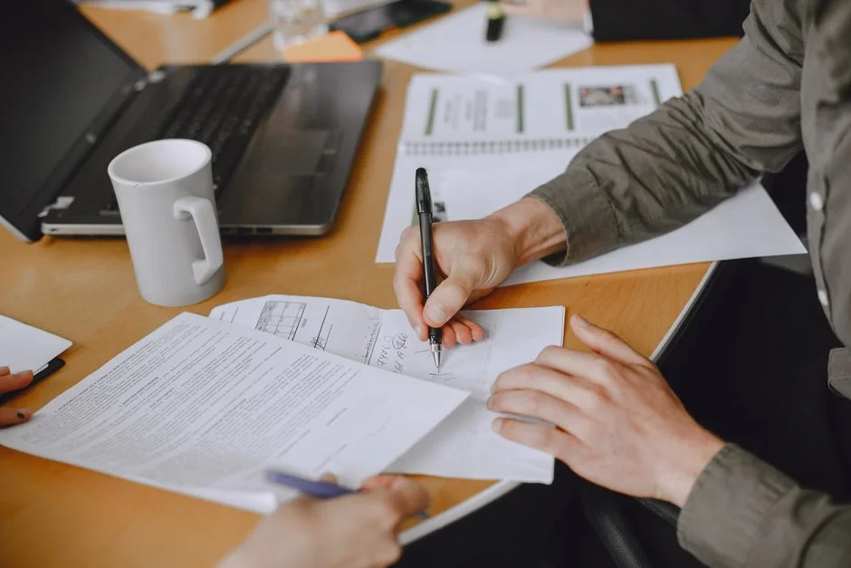 Zwei Personen sitzen am Tisch, eine unterschreibt mit einem Stift ein mehrseitiges Dokument