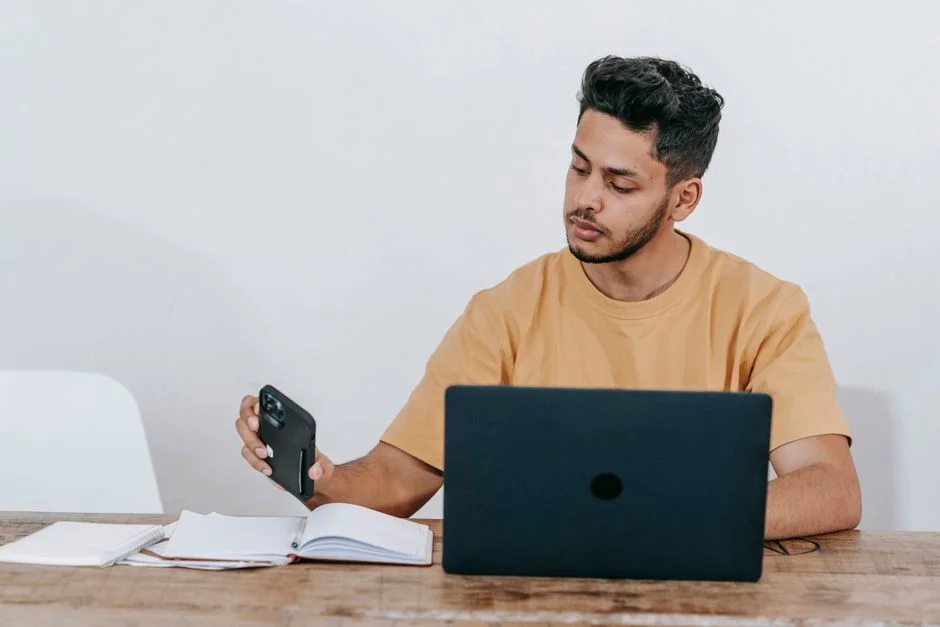 Unternehmer prüft am Laptop eine Nachricht auf dem Smartphone