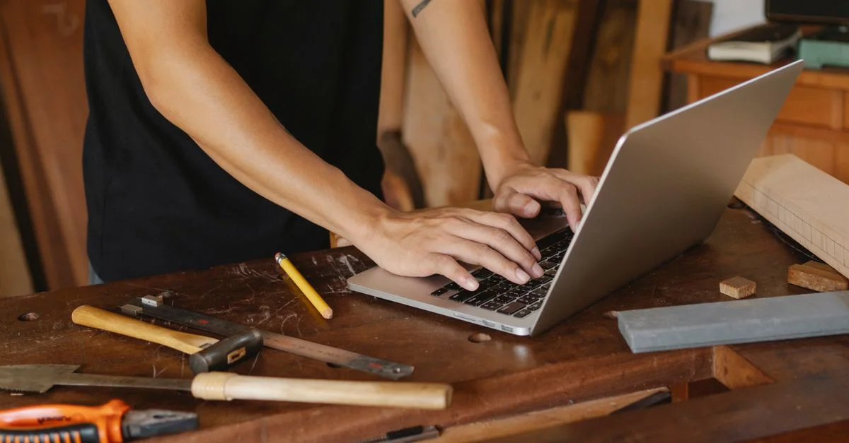 Handwerker prüft Website-Informationen am Laptop zwischen Werkzeugen